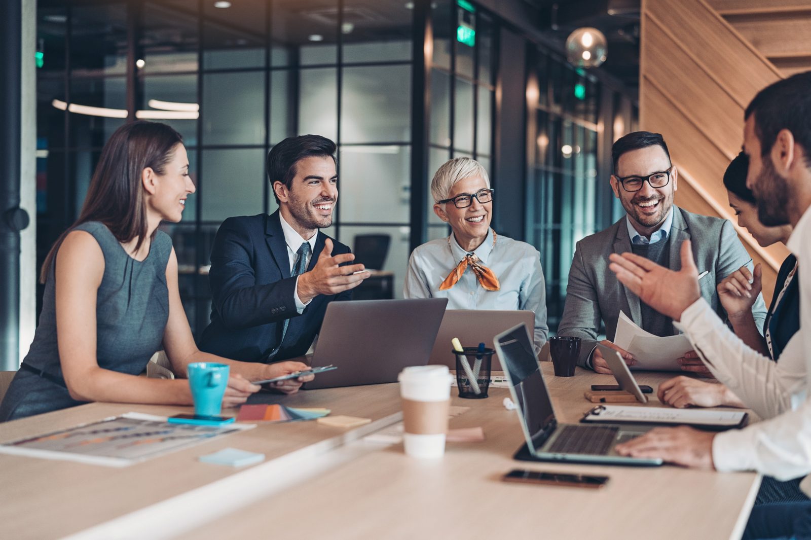 A diverse group of professionals leaning into a relaxed, engaged conversation around a boardroom table.